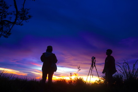 hiker with camera making photo on a hill at sunset and clouded skyの写真素材