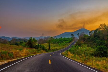 Highway road up hill through green grass field under white clouds on blue sky in summer day. Road trip travel conceptの写真素材