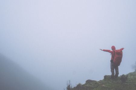 man with backpack standing on a hill in foggy weatherの写真素材