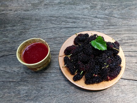 Close up group of mulberries is placed on a wooden spoon in front of a glass of mulberries juice. Mulberry this a fruit and can be eaten. Mulberry is delicious and sweet nature. Copy Spaceの写真素材