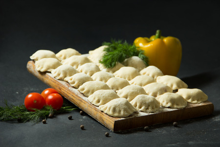 dumplings on a black background with fresh herbs and vegetables. homemade food. Traditional Russian food is pelmeni.の写真素材