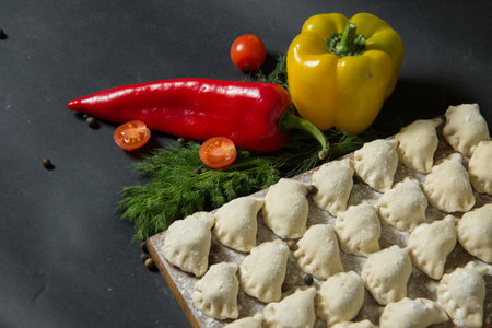 dumplings on a cutting board. raw dumplings on a black background. Vegetables with dumplings on the kitchen tableの写真素材