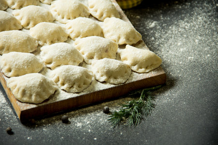 dumplings on a cutting board. raw dumplings on a black background. Vegetables with dumplings on the kitchen tableの写真素材