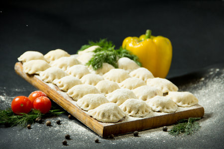 dumplings on a cutting board. raw dumplings on a black background. Vegetables with dumplings on the kitchen tableの写真素材