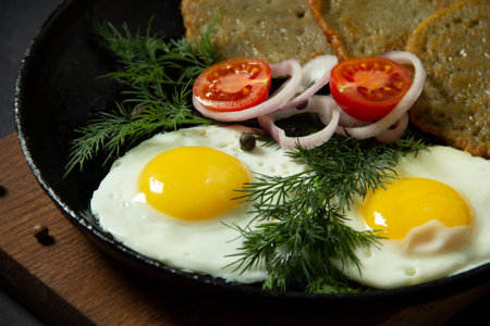 hot fried eggs with greens and vegetables on a black backgroundの写真素材
