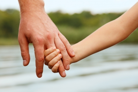 father's hand lead his child son against summer forest and river nature outdoor background, trust family conceptの写真素材