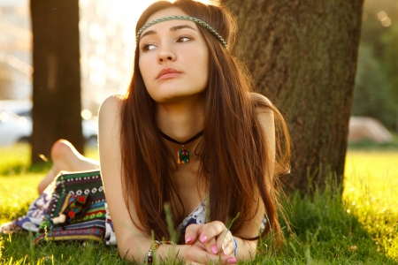 Outdoors warm summer portrait of beautiful young girl lying on green grass near treeの写真素材