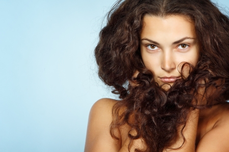 Beauty portrait of beautiful cheerful young fresh woman with long brown healthy curly hair. Isolated on blue background の写真素材