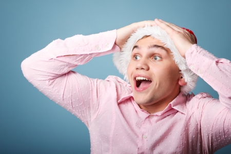 surprise young cheerful christmas man with santa's hat over blue backgroundの写真素材