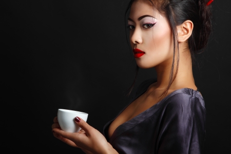 Young beautiful asian woman and tea ceremony, studio shot over black backround with copyspaceの写真素材