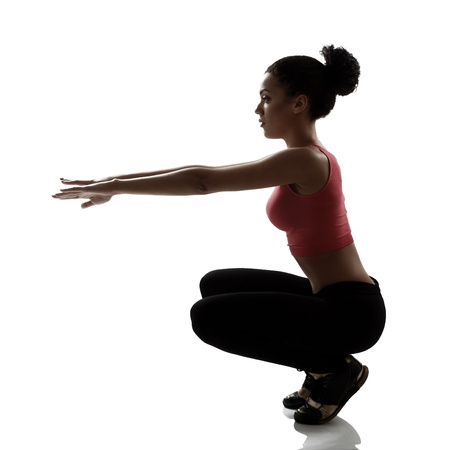 sport young woman athlete doing squatting exercise, active fitness girl silhouette studio shot over white backgroundの写真素材