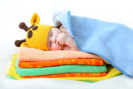 cute sleeping baby boy in funny hand made giraffe hat, beautiful kid dozing on pile of colorful towels with blue plaid, studio shotの写真素材