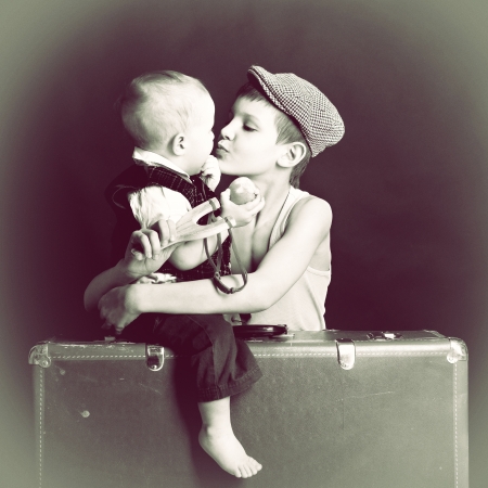 vintage art portrait of little boy hugs and kiss his baby brother leaning on old suitcase, retro stylization of 30-50s, tonedの写真素材