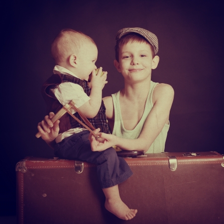 vintage art portrait of little boy eating an apple with his baby brother leaning on old suitcase, retro stylization of 30-50sの写真素材