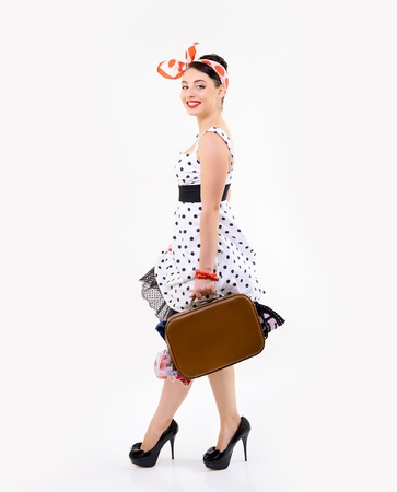 Pinup girl with suitcase in dress spotted, full length portrait of young happy sexy woman in pin-up style, retro stylization over whiteの写真素材