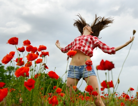 Young beautiful woman walking and dancing through a poppy field, summer outdoor.の写真素材
