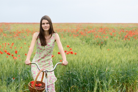 Young beautiful woman with bicycle and basket with cherry on a poppy field, summer outdoor.の写真素材