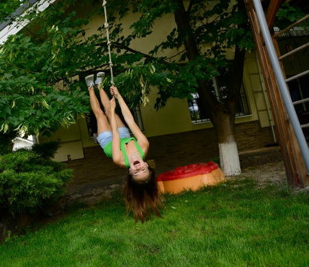 Happy excited teen girl on a swing upside down, summer park garden outdoorの写真素材