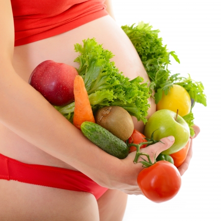 Beautiful pregnant woman in red with fresh fruits and vegetables, healthy life concept, isolated over a white background の写真素材