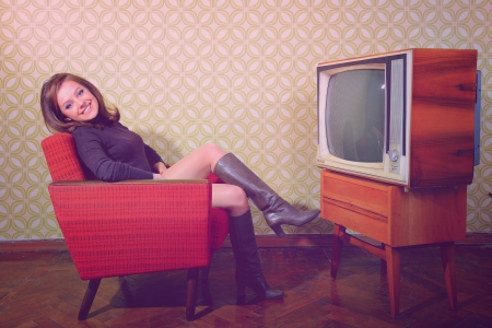 portrait of young smiling woman sitting in vintage room and watching tv, retro stylization, toned and noise addedの写真素材