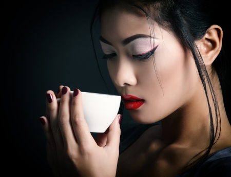 Young beautiful asian woman and tea ceremony, studio shot over black backround with copyspaceの写真素材