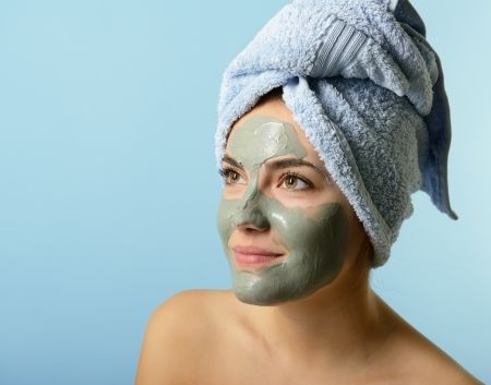 Beautiful young woman with clay facial mask, beauty treatment over blueの写真素材