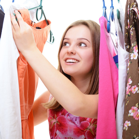 Portrait of a happy attractive teen girl making choices in wardrobe or in shop with clothesの写真素材