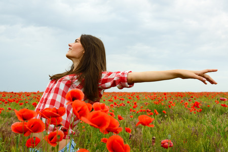 Young beautiful woman walking and dancing through a poppy field, summer outdoor.の写真素材