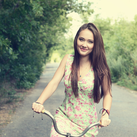 Happy young beautiful woman with retro bicycle. Portrait of fresh girl with cycle over summer outdoor, image toned.の写真素材