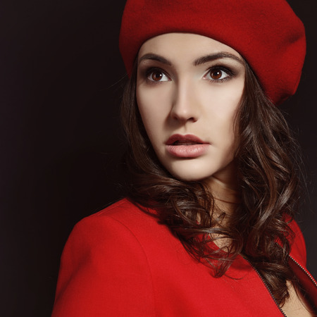 Stylish fashion girl in red suit and beret with, posing at studio over black backgroundの写真素材
