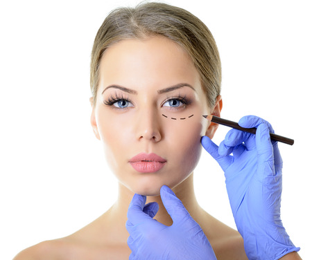 Beautiful woman ready for cosmetic surgery, female face with doctor's hands with pencil, over whiteの写真素材