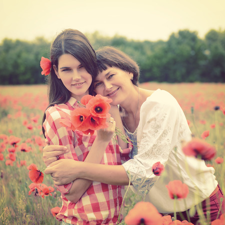Attractive middle-aged woman have fun on a poppy field with her, summer outdoor. の写真素材