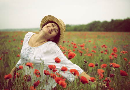 Cheerful attractive woman has fun on a poppy field, summer outdoor. Image toned.の写真素材