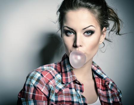 Beautiful teen girl inflating bubble of chewing gum. Moderm fashion girl. Toned.の写真素材