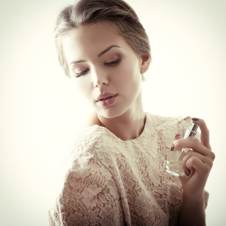Girl with perfume, young beautiful woman holding bottle of perfume and smelling aroma, tonedの写真素材