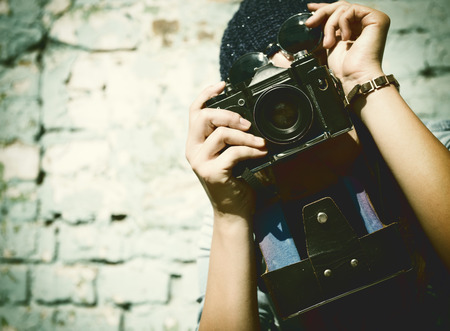 urban girl has fun with vintage photo camera outdoor near grunge wall, image toned.の写真素材
