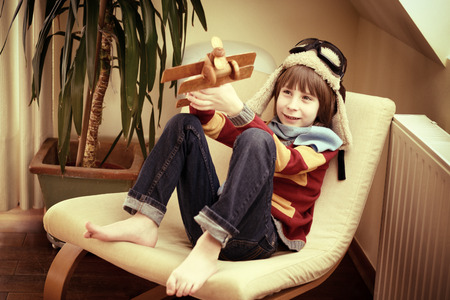 Little boy aviator dreaming and playing with wooden handmade toy plane at home, vintage tonedの写真素材