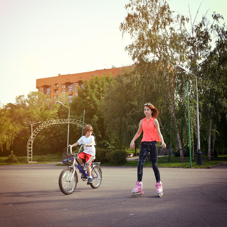 Teen girl on roller skates smiling and little boy bike on bicycle behind. Toned.の写真素材