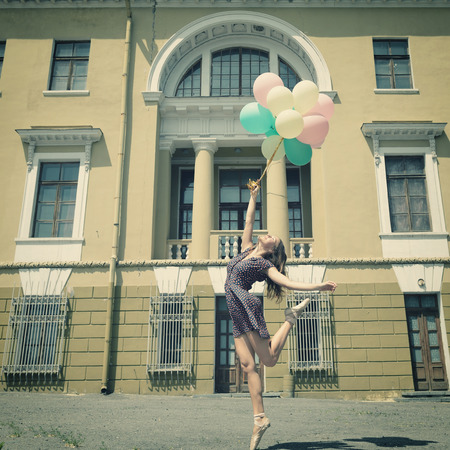 Attractive teen girl dancing with ballons outdoor against old building. Vintage toned.の写真素材