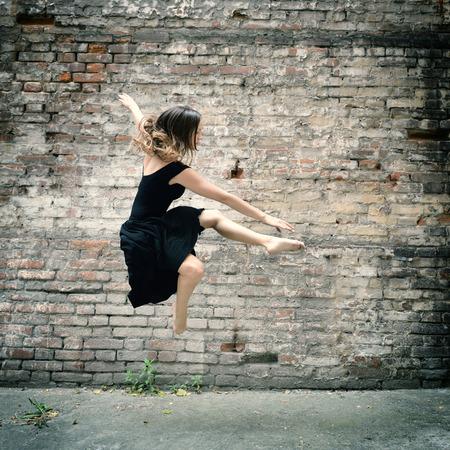 Attractive teen girl dancing outdoor against grunge bricks wall. Toned.の写真素材