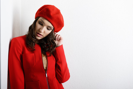 Stylish fashion girl in red suit and beret, posing at studio over white wallの写真素材