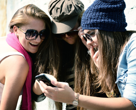 Girls having fun together outdoors using smart phone, lifestyle. 