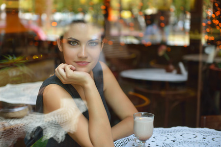 Young beautiful woman sitting in cafe, drinking coffee. Image toned, noise added.の写真素材