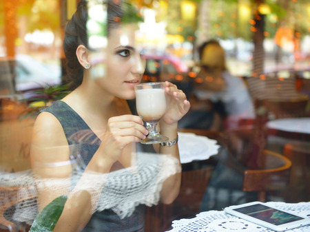 Young beautiful woman sitting in cafe, drinking coffee and using her smartphone. Image toned, noise...