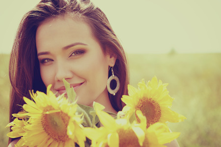 Young beautiful woman enjoying summer, youth and freedom, holding sunflowers against blue sky. Image toned.の写真素材