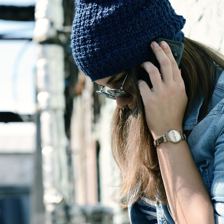 Teen girl calling smart phone outdoor. Teenage problem. Image toned and noise added.の写真素材