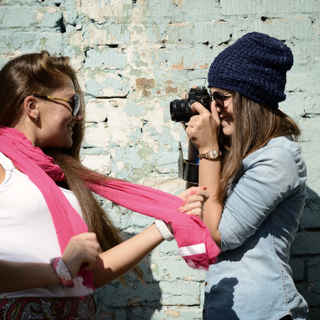 Urban girls have fun with vintage photo cameras outdoor near grunge wall, image toned and noise addedの写真素材