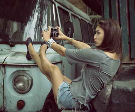 Urban girl has fun with vintage photo cameras outdoor near tree and retro car, image toned.の写真素材