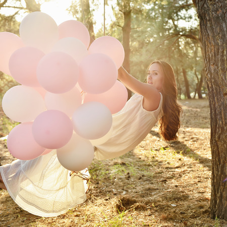 Young woman is swinging on a swing in summer pine forest. Image toned and noise added.の写真素材