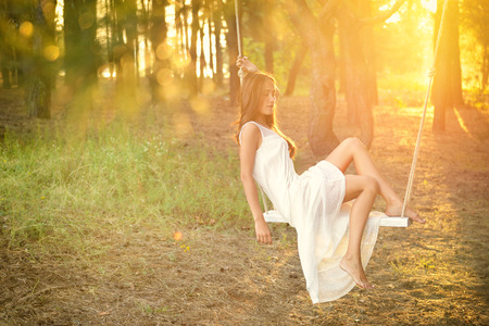 Young woman is swinging on a swing in summer pine forest. Image toned and noise added.の写真素材